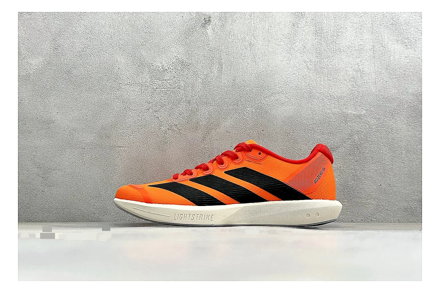 Adidas Adizero Orange Black shopping brief photo showing orange runner upper, black three-stripe contrast, lightweight racing shape, and thin performance sole